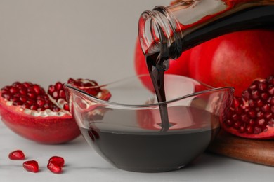Photo of Pouring tasty pomegranate sauce into bowl and fresh ripe fruit on white marble table, closeup