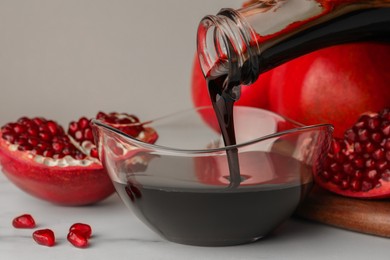 Pouring tasty pomegranate sauce into bowl and fresh ripe fruit on white marble table, closeup