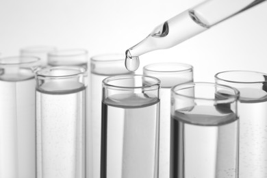 Photo of Dripping transparent liquid into test tube on white background, closeup