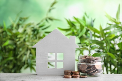 House model and jar with coins on table against blurred background. Space for text