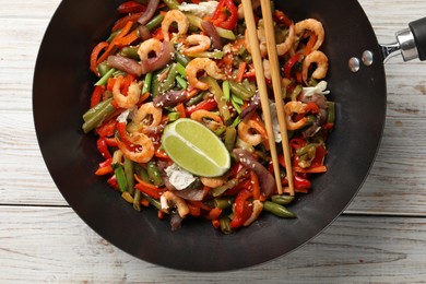 Photo of Shrimp stir fry with vegetables in wok and chopsticks on light wooden table, top view