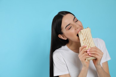 Young woman eating delicious shawarma on light blue background. Space for text
