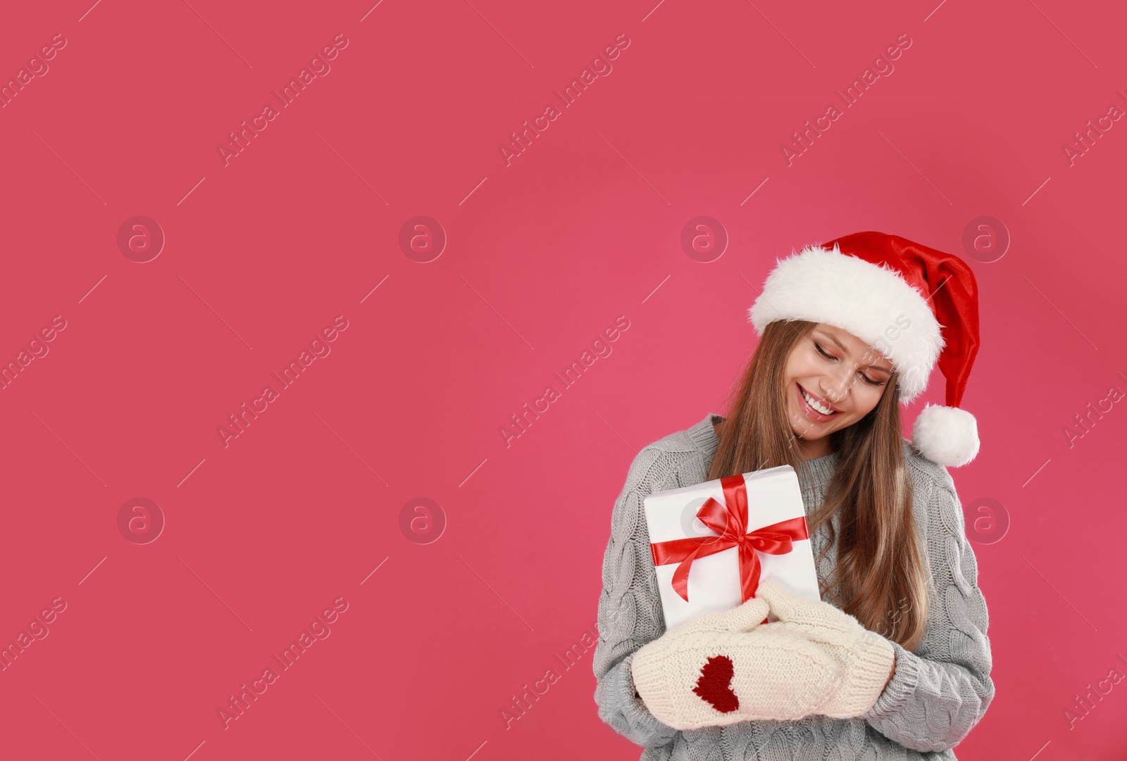 Photo of Happy young woman in Santa hat with Christmas gift on pink background. Space for text