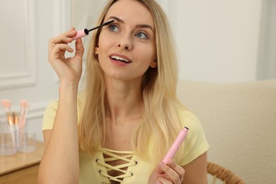 Photo of Beautiful woman applying mascara with brush at home