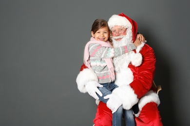 Photo of Little girl hugging authentic Santa Claus on grey background