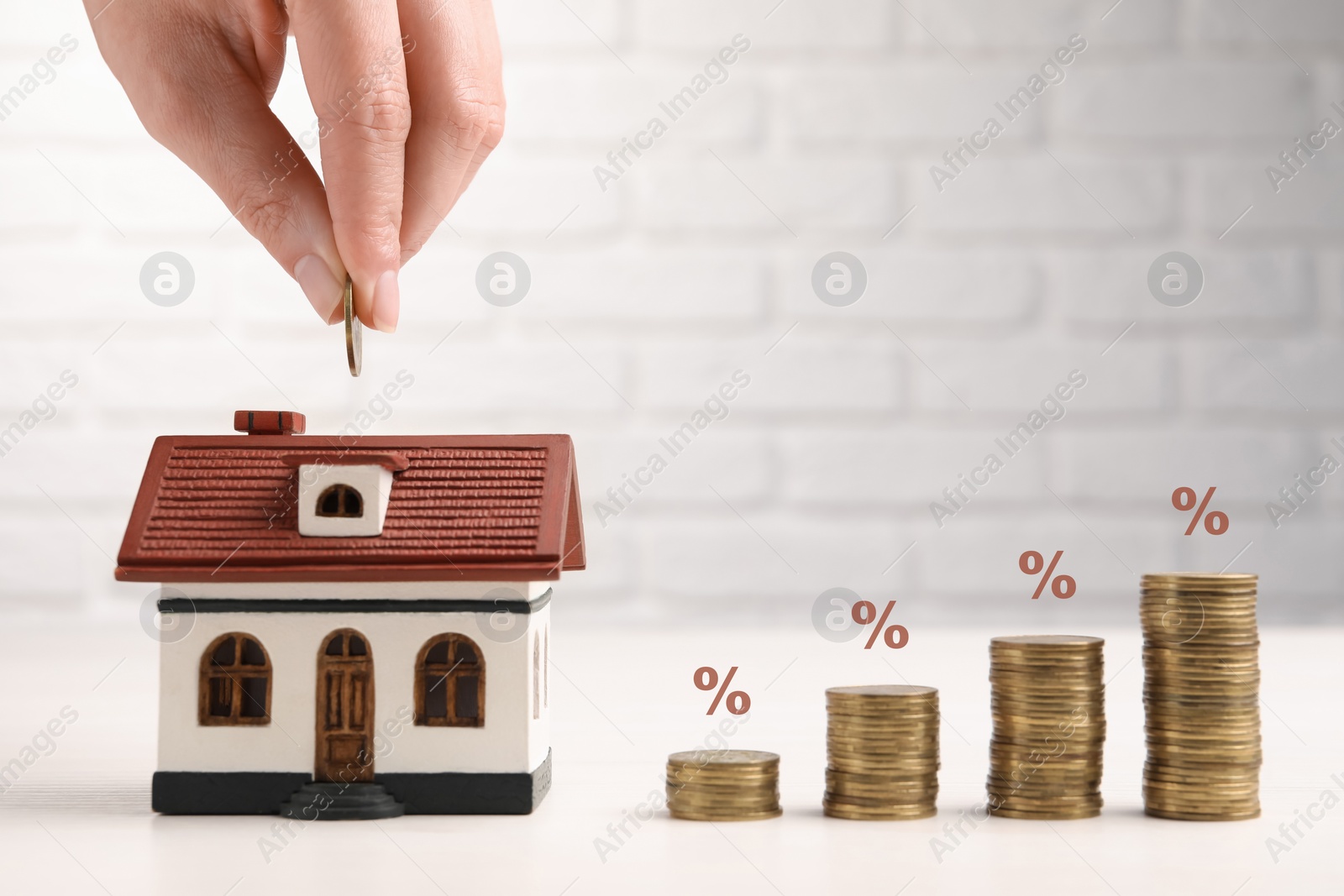 Image of Mortgage rate. Woman putting coin into house shaped money box, closeup. Stacked coins and percent signs