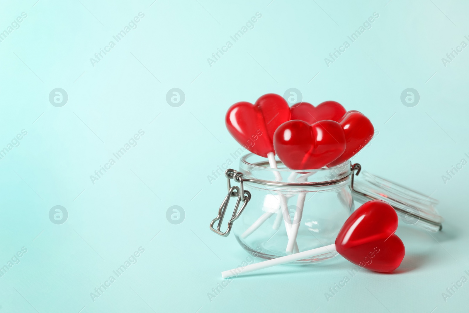 Photo of Sweet heart shaped lollipops in glass jar on light blue background, space for text. Valentine's day celebration