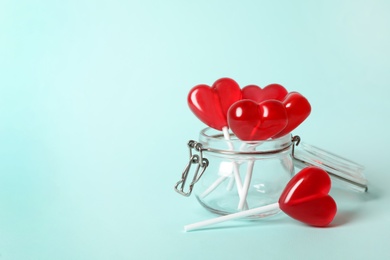 Sweet heart shaped lollipops in glass jar on light blue background, space for text. Valentine's day celebration