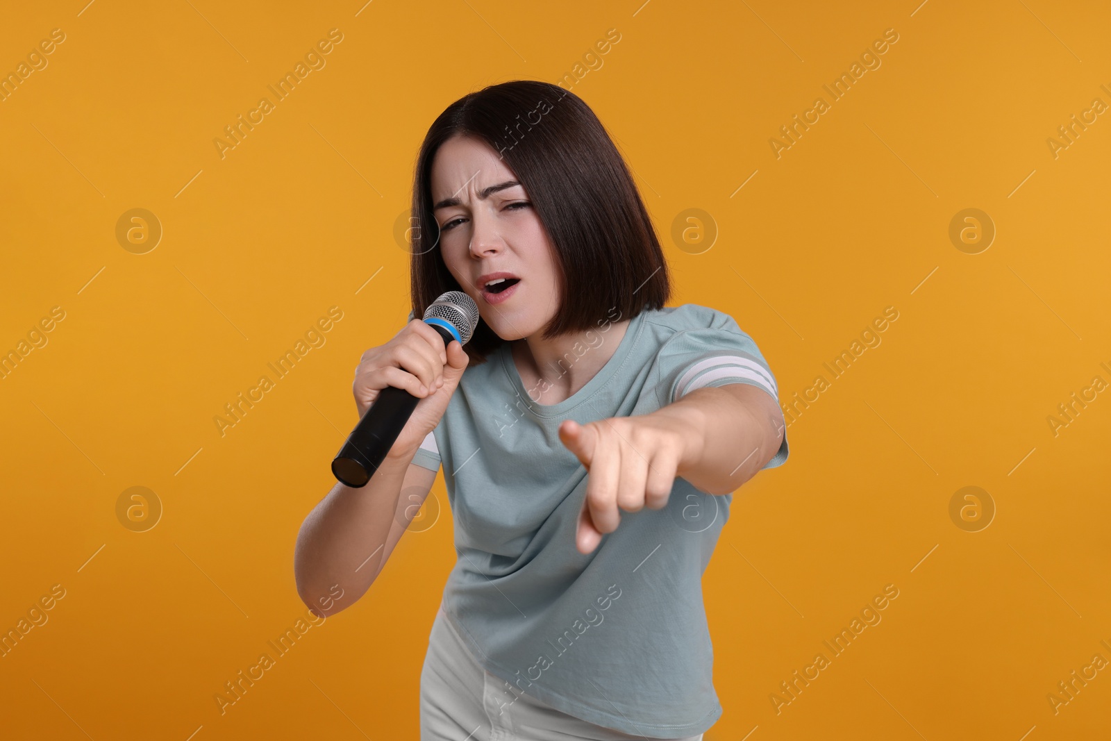 Photo of Beautiful young woman with microphone singing on yellow background