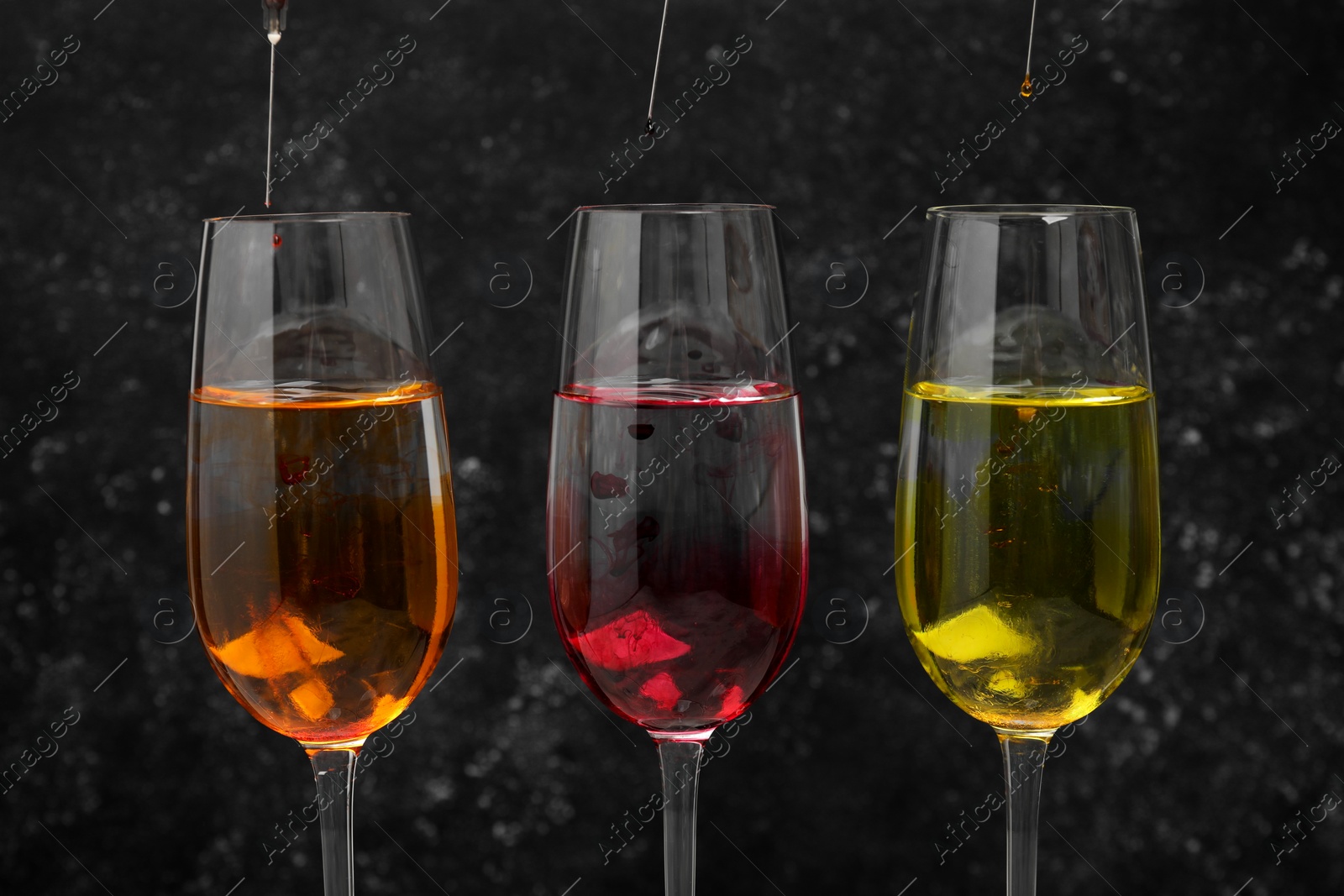 Photo of Different food coloring pouring into glasses on grey background