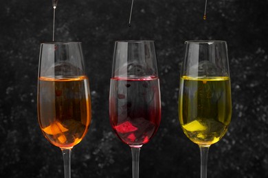 Different food coloring pouring into glasses on grey background