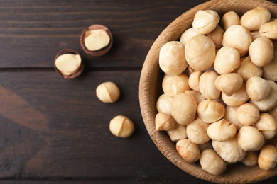 Photo of Bowl with shelled organic Macadamia nuts and space for text on wooden background, top view