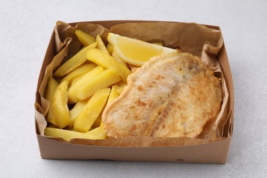 Photo of Delicious fish and chips in paper box on light gray table, closeup