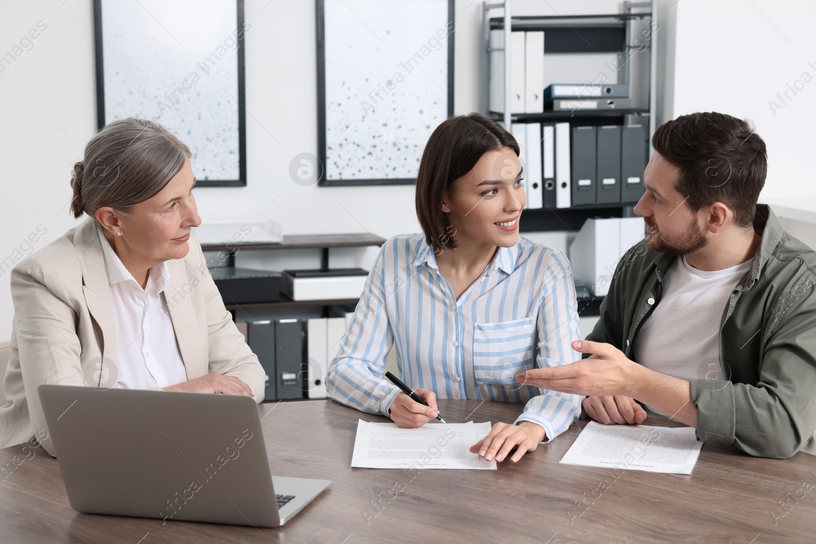 Photo of Young couple consulting insurance agent about pension plan at wooden table indoors