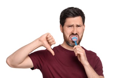 Handsome man brushing his tongue with cleaner and showing thumb down on white background