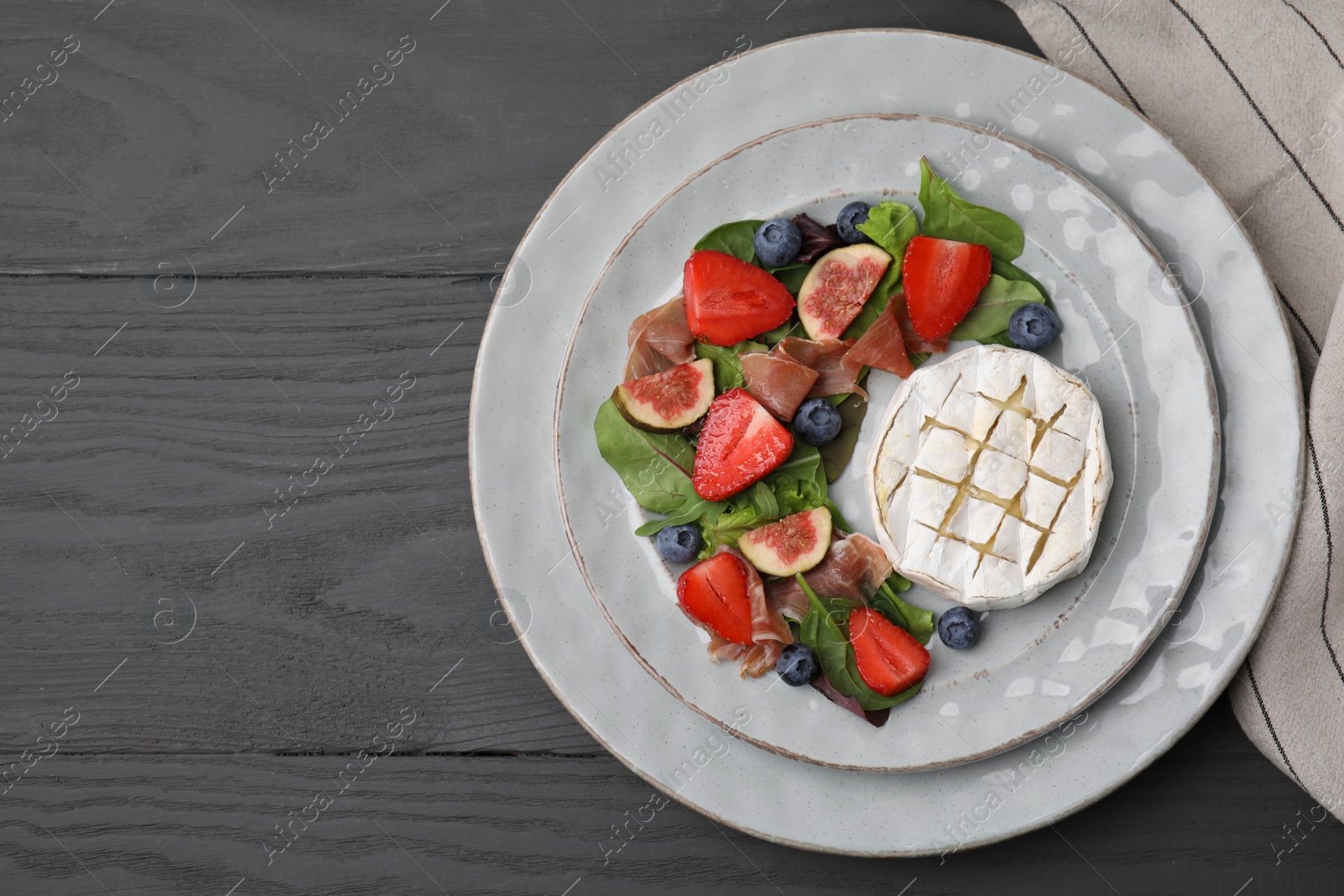 Photo of Delicious salad with brie cheese, prosciutto, figs and strawberries on grey wooden table, top view. Space for text