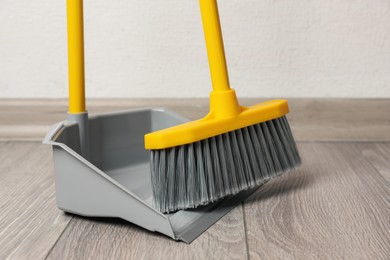 Photo of Plastic broom with dustpan on wooden floor indoors