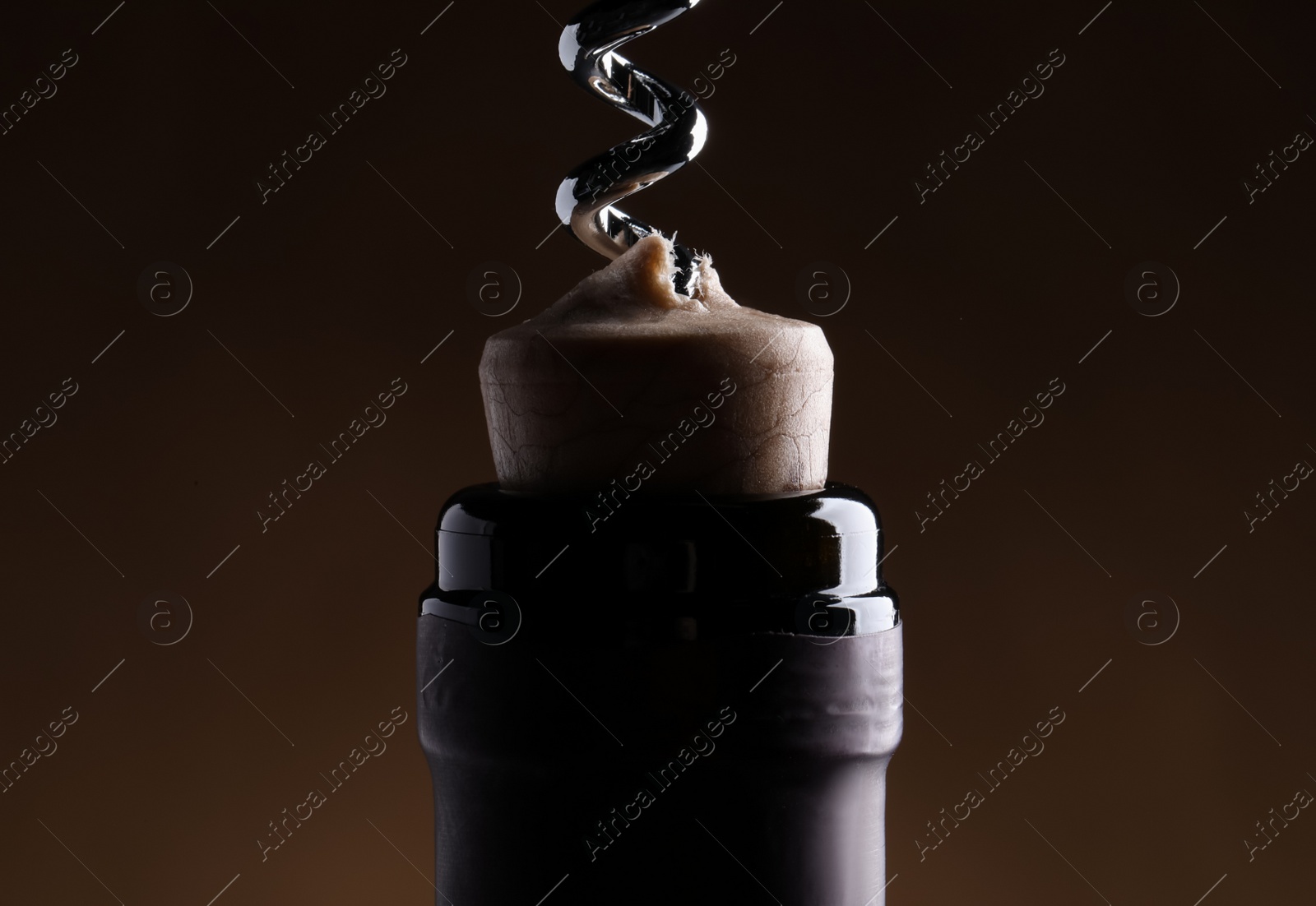 Photo of Opening wine bottle with corkscrew on dark brown background, closeup