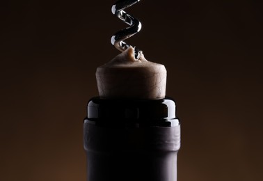 Photo of Opening wine bottle with corkscrew on dark brown background, closeup