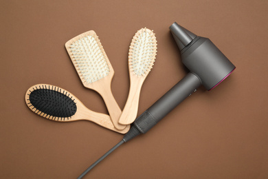 Hair dryer and different brushes on brown background, flat lay. Professional hairdresser tool