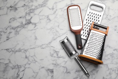 Photo of Different modern graters on white marble table, flat lay. Space for text