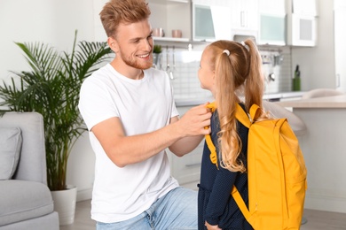 Happy father helping little child to put on school bag at home