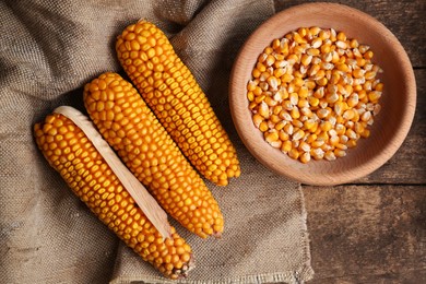 Delicious ripe corn cobs and bowl with seeds on wooden table, flat lay