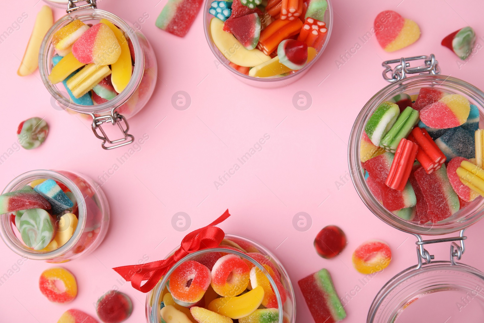 Photo of Frame made of glass jars with tasty colorful jelly candies on pink background, flat lay. Space for text