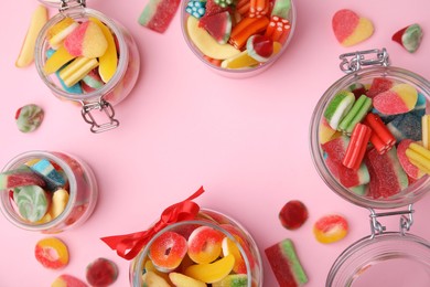 Photo of Frame made of glass jars with tasty colorful jelly candies on pink background, flat lay. Space for text