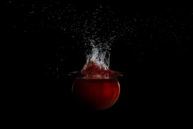 Pomegranate falling down into clear water against black background