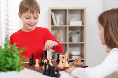 Cute children playing chess at table in room