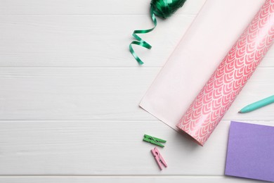 Photo of Rollfestive wrapping paper, ribbon, card, pen and clothespins on white wooden table, flat lay. Space for text
