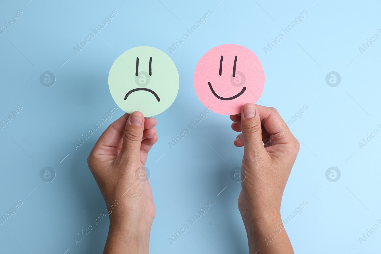 Photo of Choice concept. Woman holding papers with sad and happy emoticons on light blue background, top view