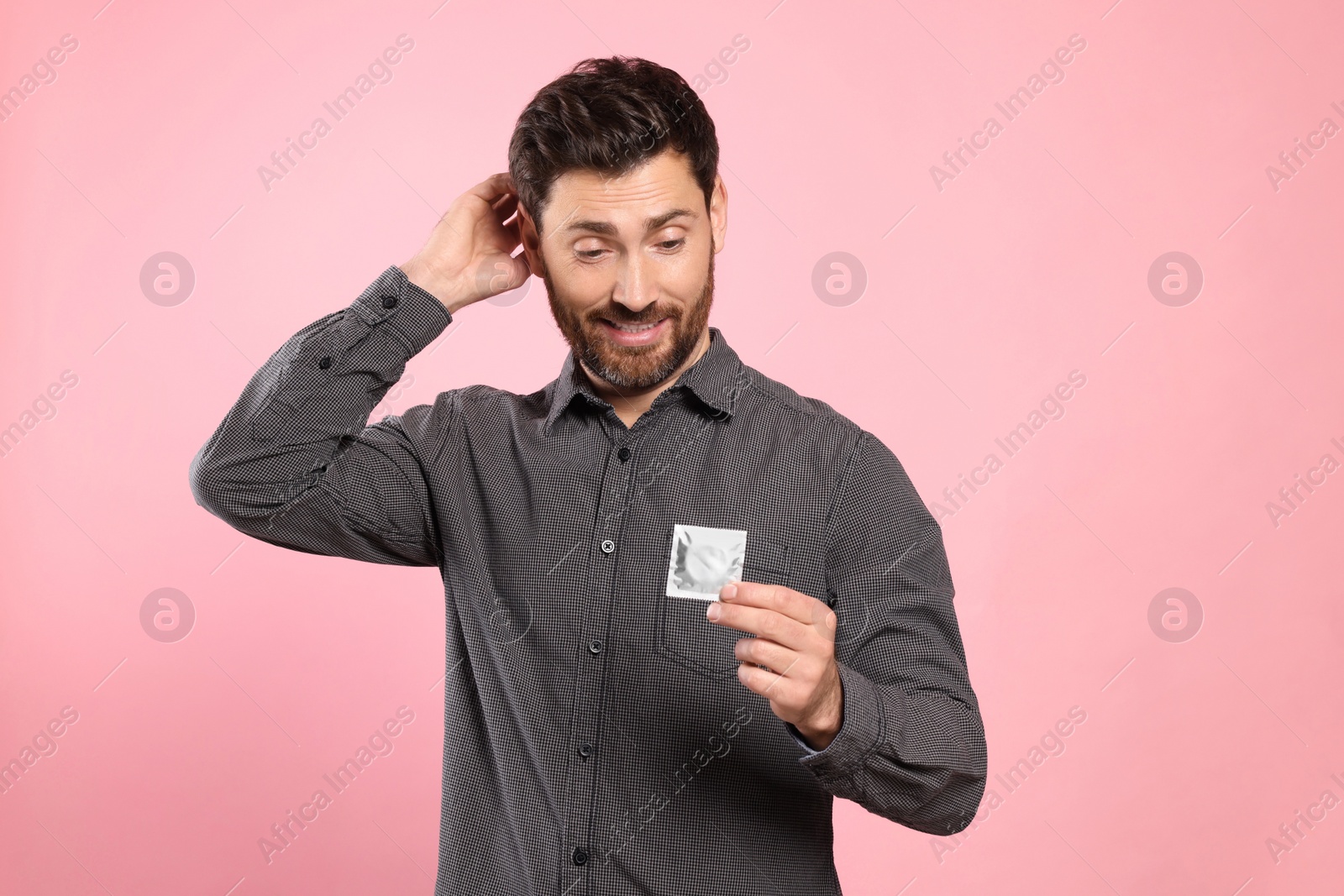 Photo of Confused man holding condom on pink background. Safe sex