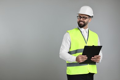 Engineer in hard hat holding clipboard on grey background, space for text