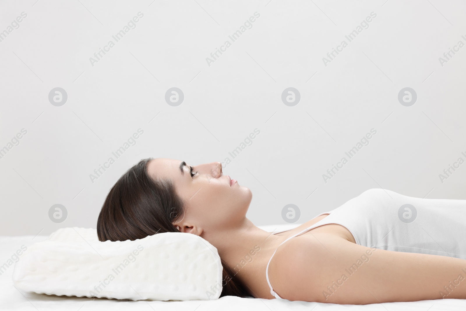 Photo of Woman lying on orthopedic pillow against light grey background, space for text