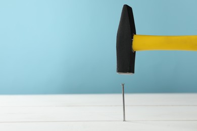 Photo of Hammering metal nail on white wooden table against light blue background. Space for text