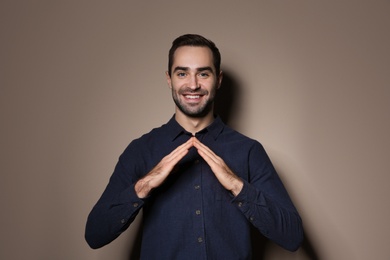 Photo of Man showing HOUSE gesture in sign language on color background