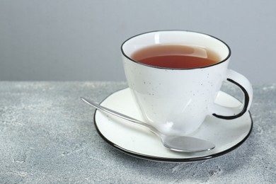 Photo of Aromatic tea in cup and spoon on grey table. Space for text