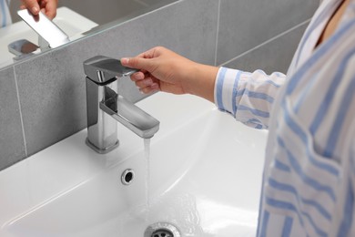 Photo of Woman opening water tap in bathroom, closeup