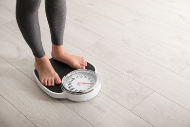 Photo of Woman standing on scales indoors, space for text. Overweight problem