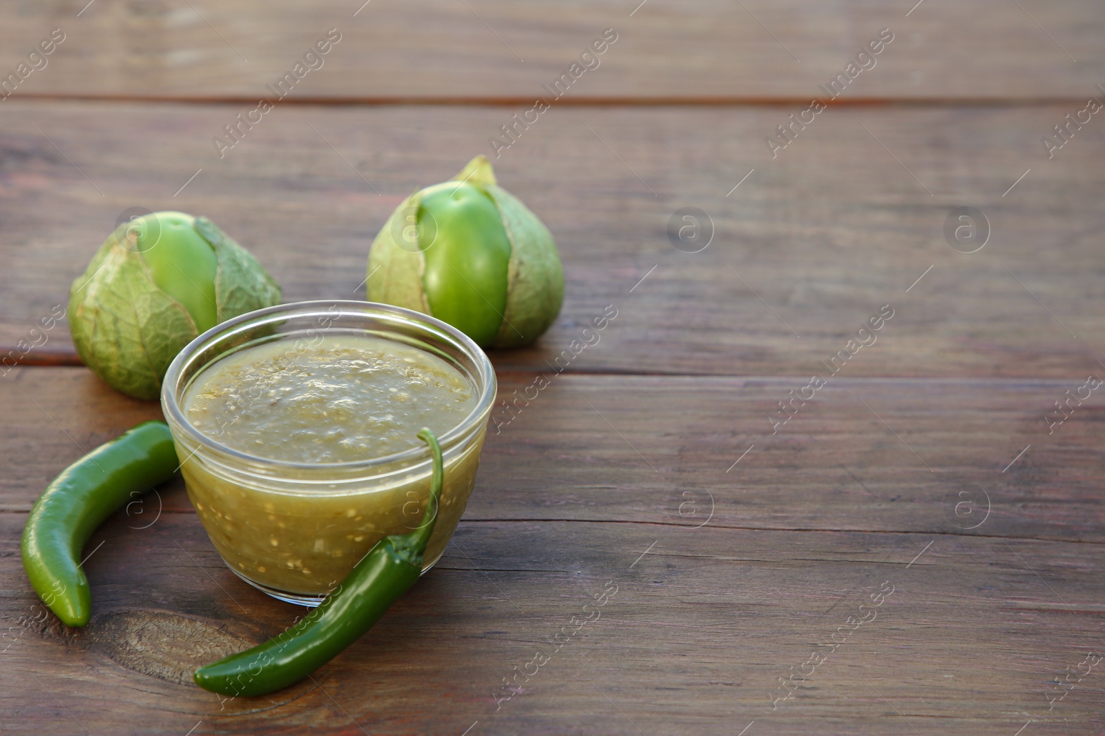 Photo of Tasty salsa sauce and ingredients on wooden table. Space for text