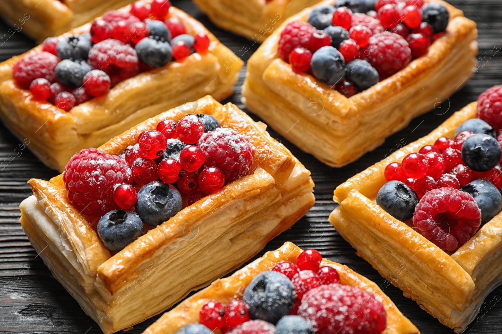 Photo of Fresh delicious puff pastry with sweet berries on dark wooden table, closeup