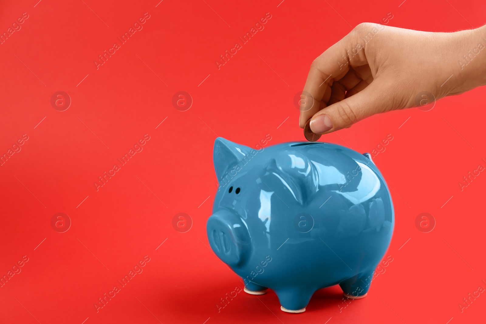 Photo of Woman putting coin into piggy bank on red background, closeup. Space for text