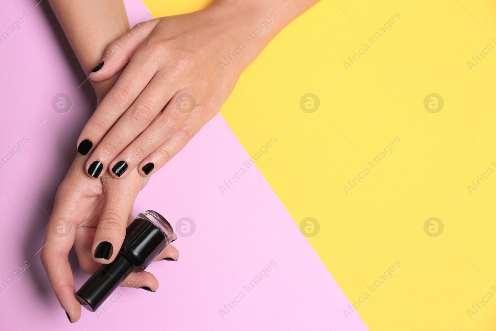 Photo of Woman with black manicure holding nail polish bottle on color background, top view. Space for text