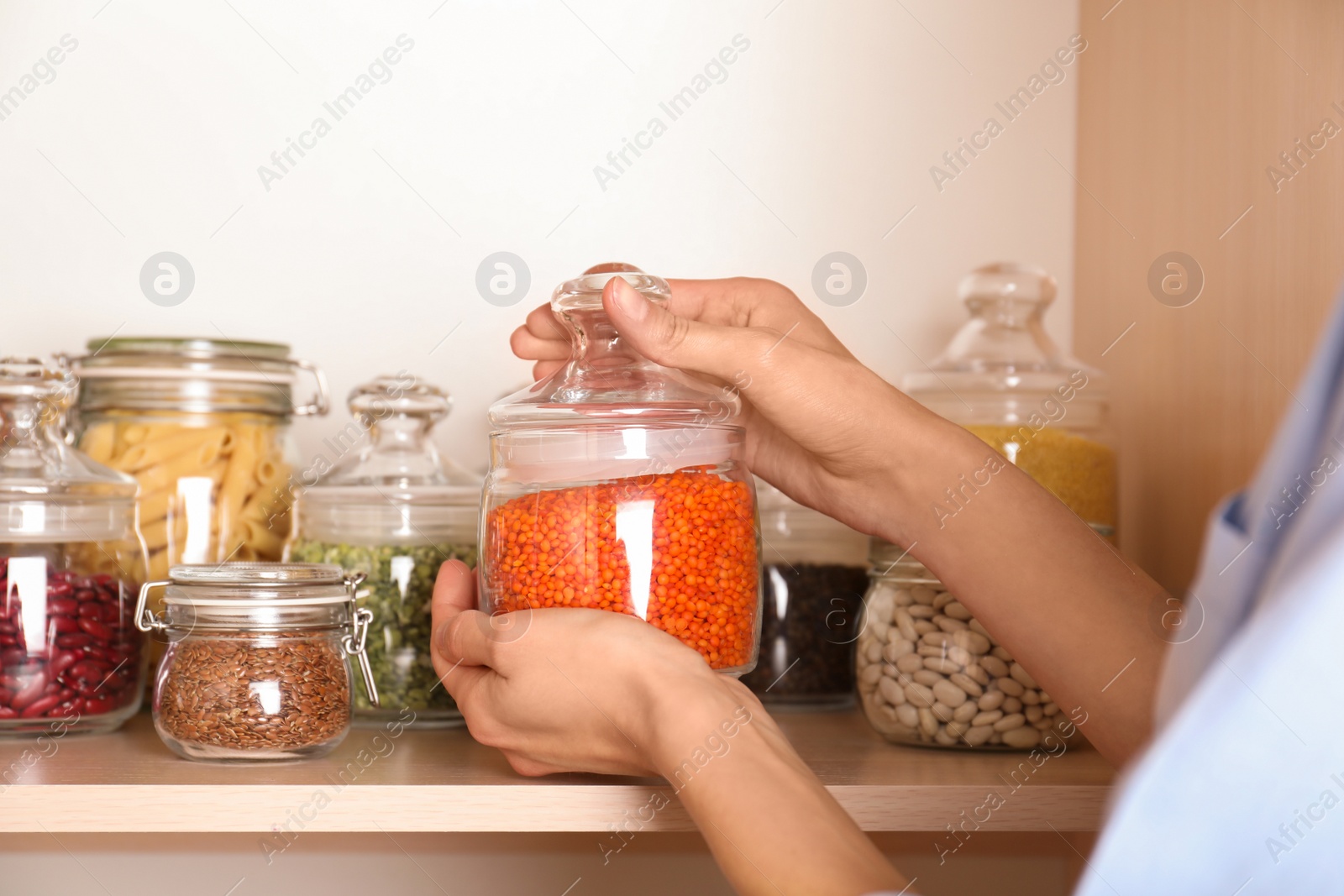 Photo of Woman taking jar of red lentil from wooden shelf, closeup