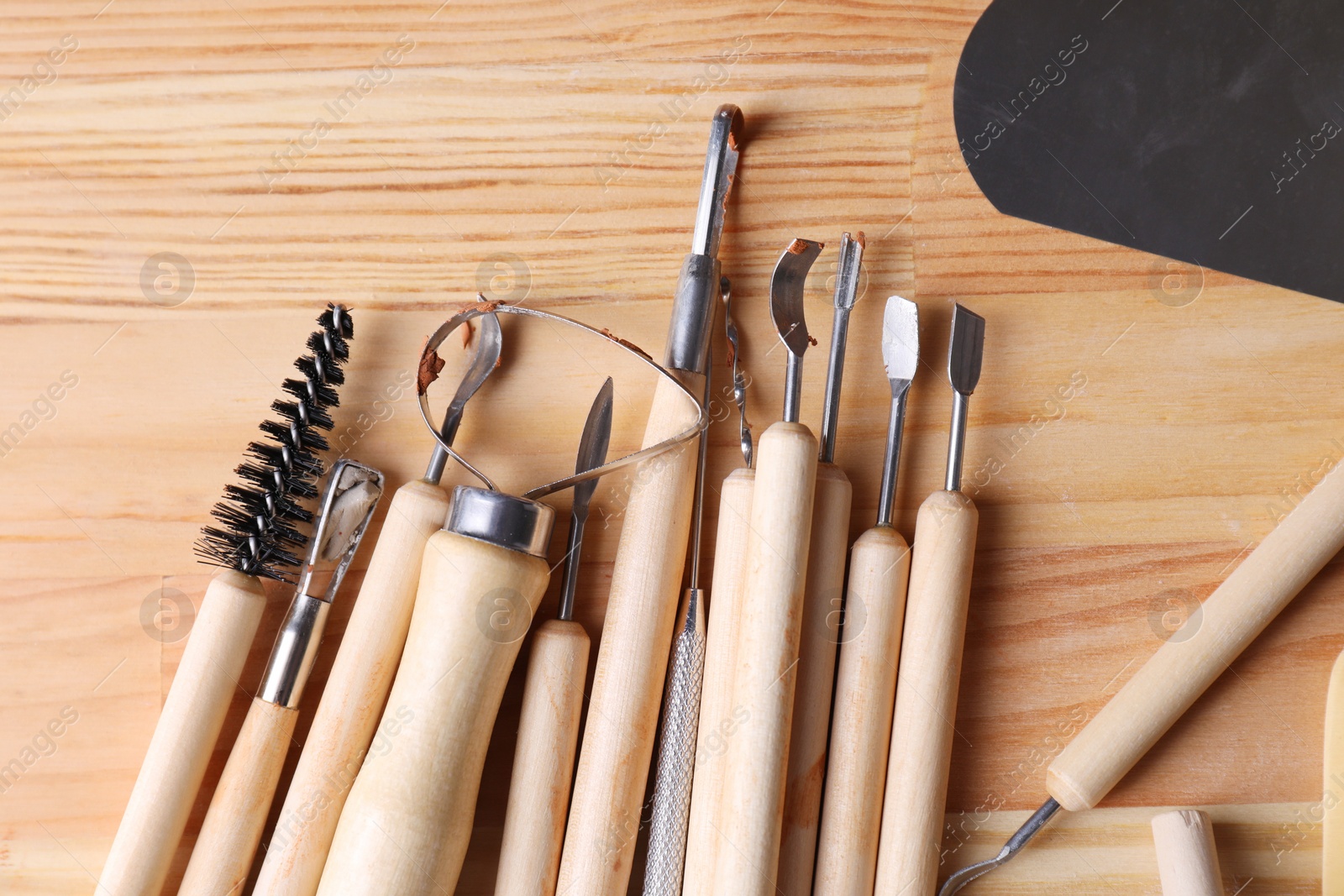 Photo of Set of different clay crafting tools on wooden table in workshop, flat lay