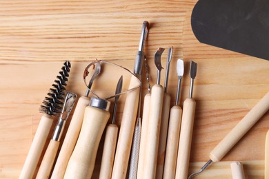 Photo of Set of different clay crafting tools on wooden table in workshop, flat lay