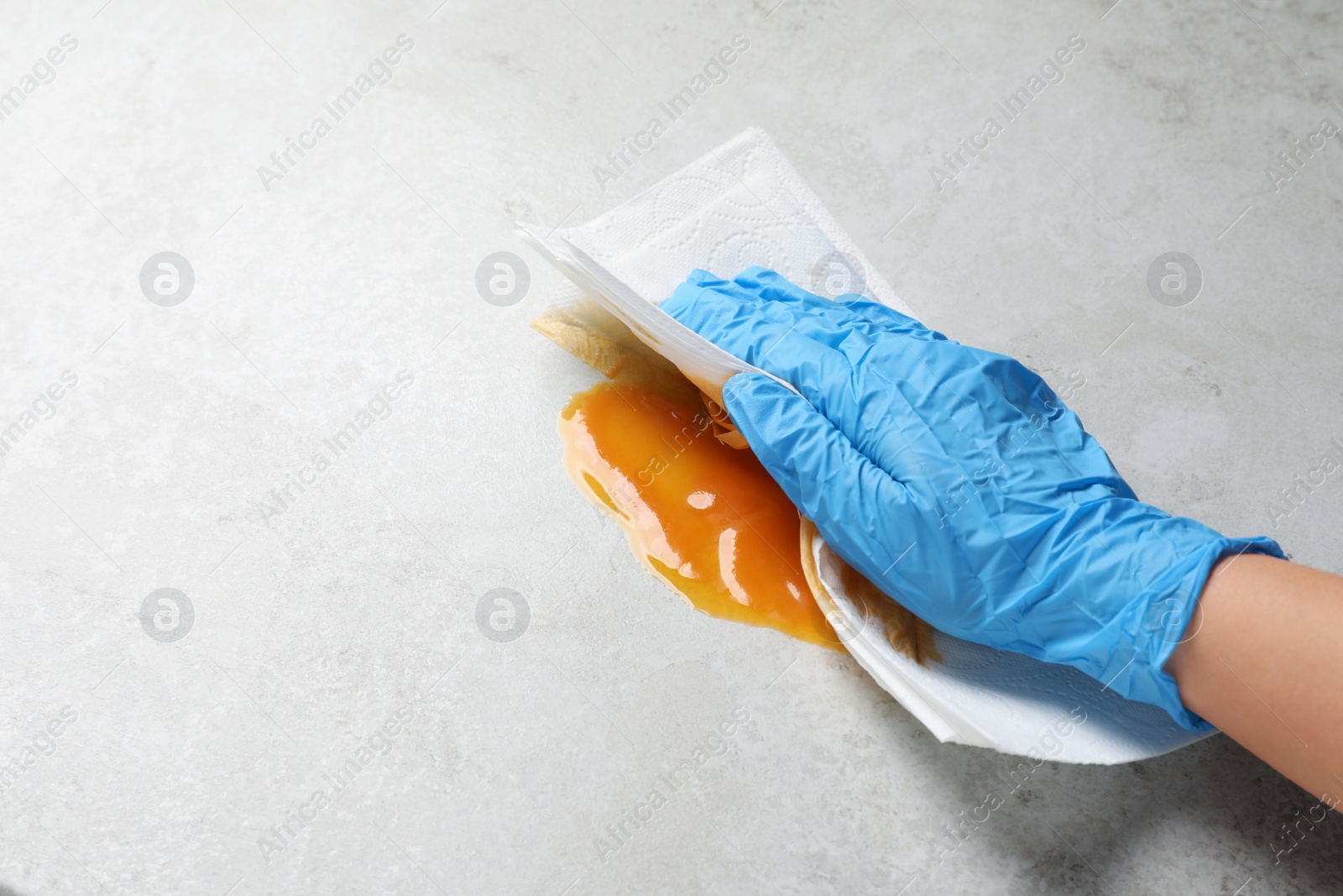 Photo of Woman wiping spilled sauce with paper towel on grey surface, closeup. Space for text