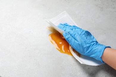 Photo of Woman wiping spilled sauce with paper towel on grey surface, closeup. Space for text